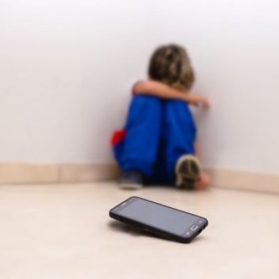 Upset child sits away from cell phone device 